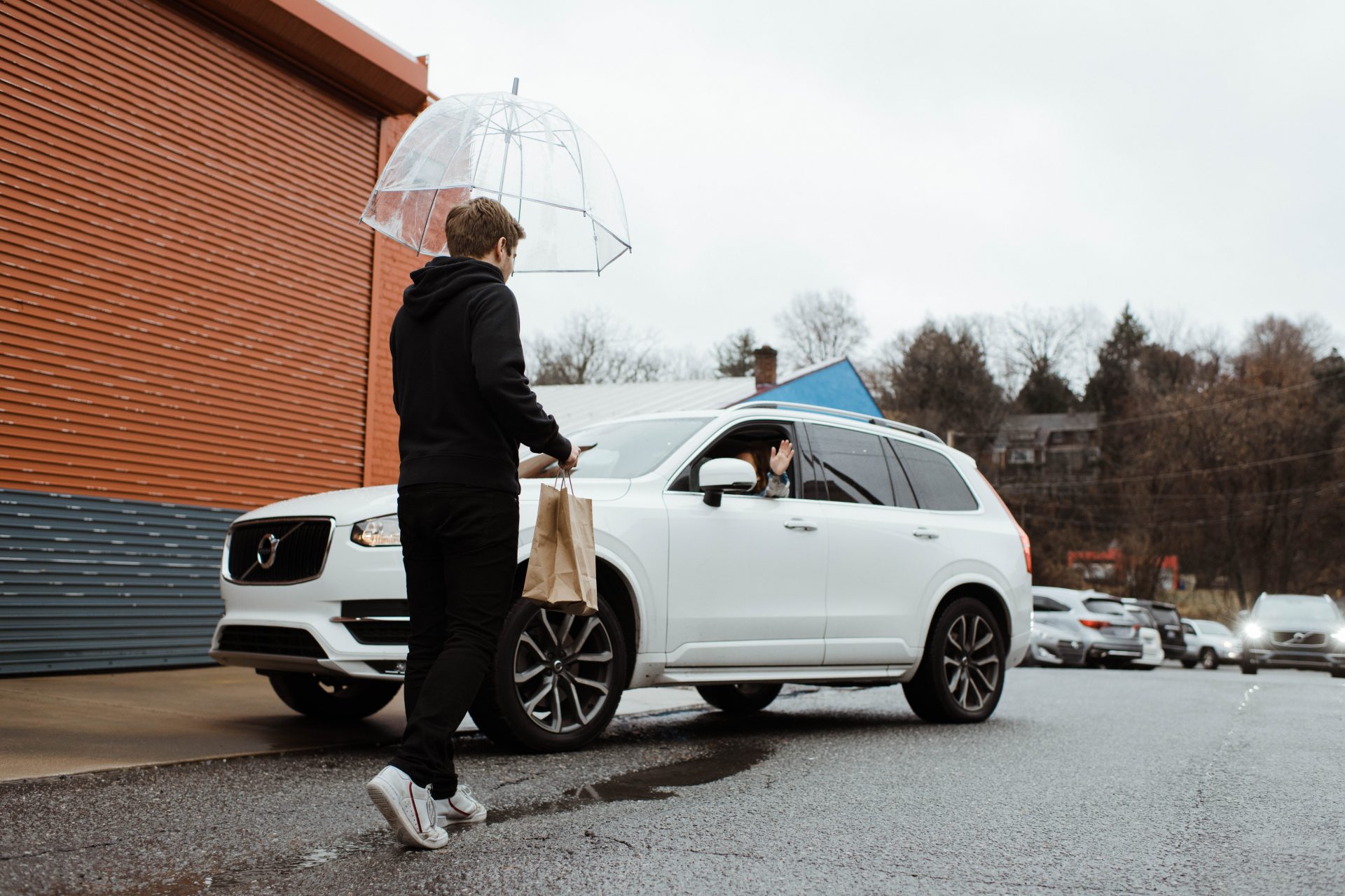 A restaurant employee walks in the rain to a white car to hand off a mean ordered from the Swipeby app.