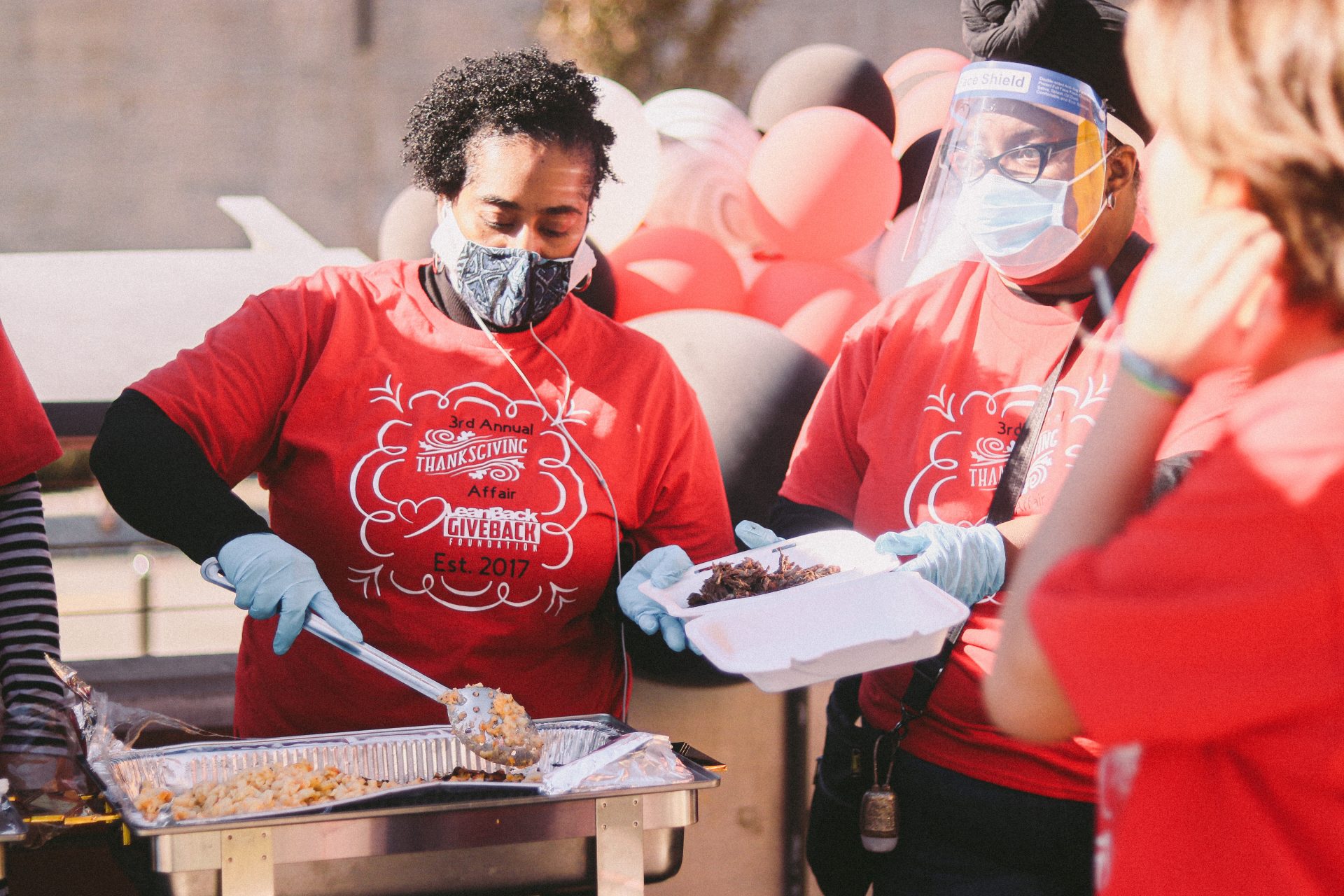 A woman in a mask puts food into a styrofoam tray during the 2021 LeanBack Give Back Thanksgiving event.